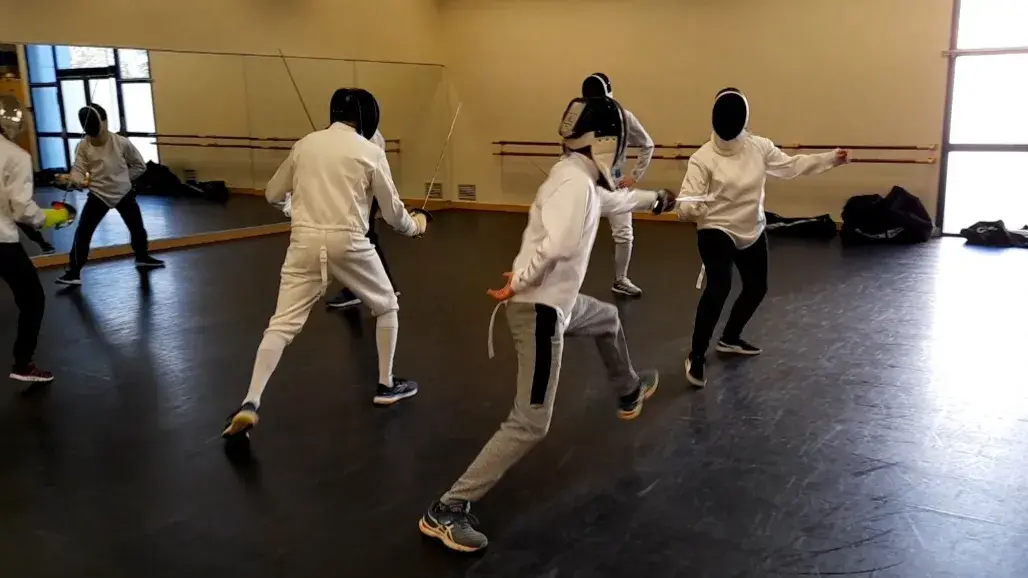 Assaut de sabre laser : un pratiquant bondit, lames bleue et verte en mouvement.